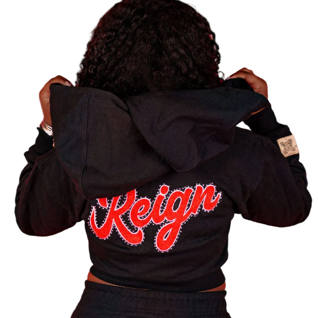 Person wearing a black jacket with 'Reign' patch on the back against a red background